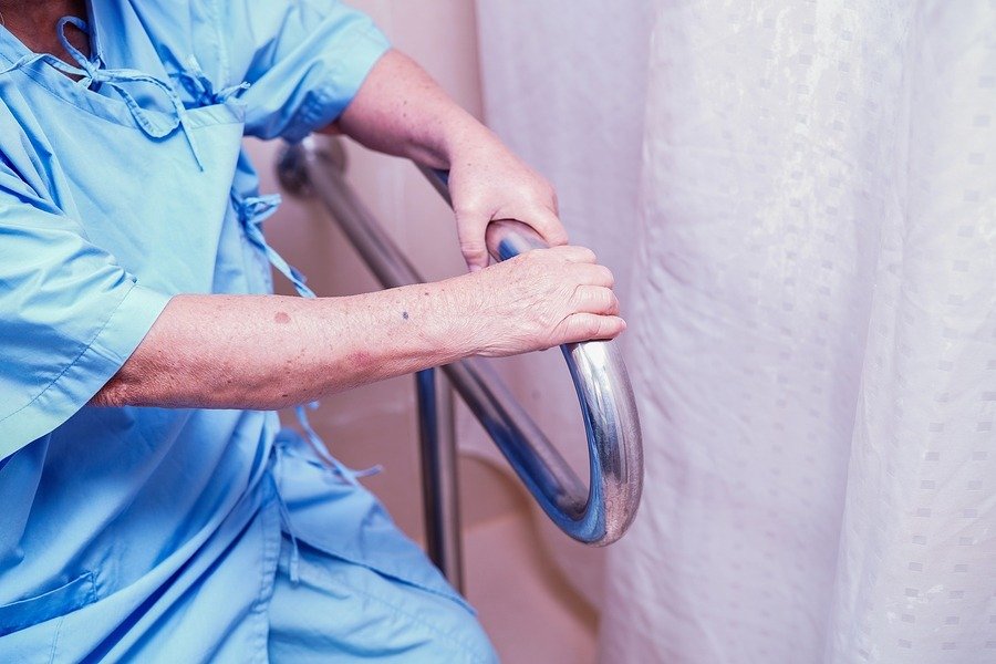 Hands gripping a safety bar in a bathroom.