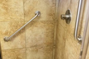 Shower with grab bar and toiletries on shelf.